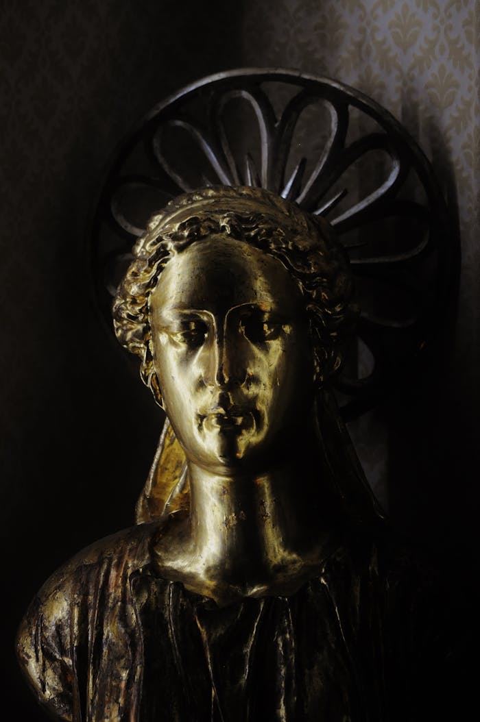 A gilded sculpture of a serene face with a halo against a textured backdrop.